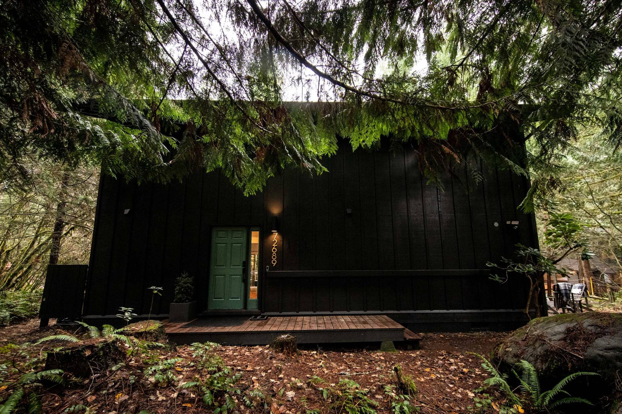 Hood Hideaway, a black cabin with a teal front door among tall firs in Rhododendron, Oregon