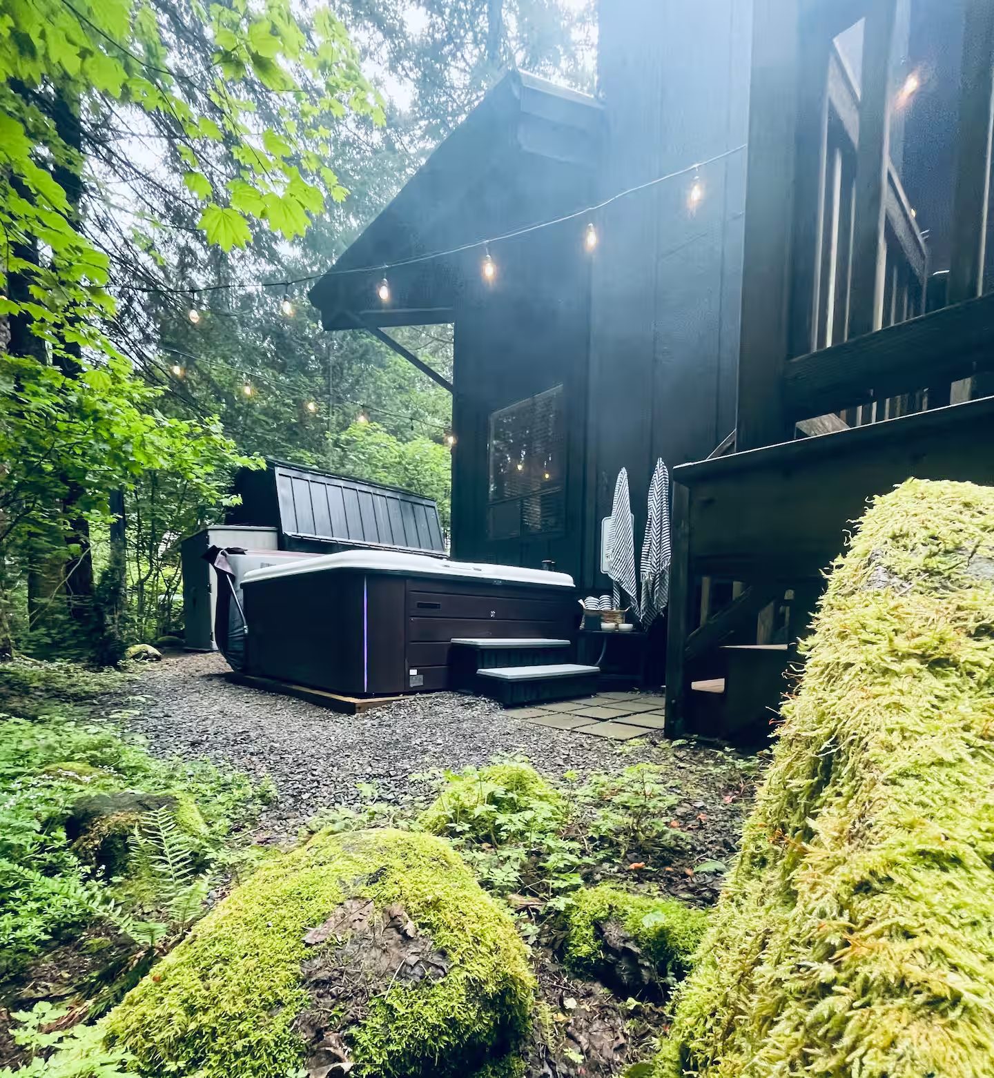 Private hot tub behind the cabin among mossy rocks and firs