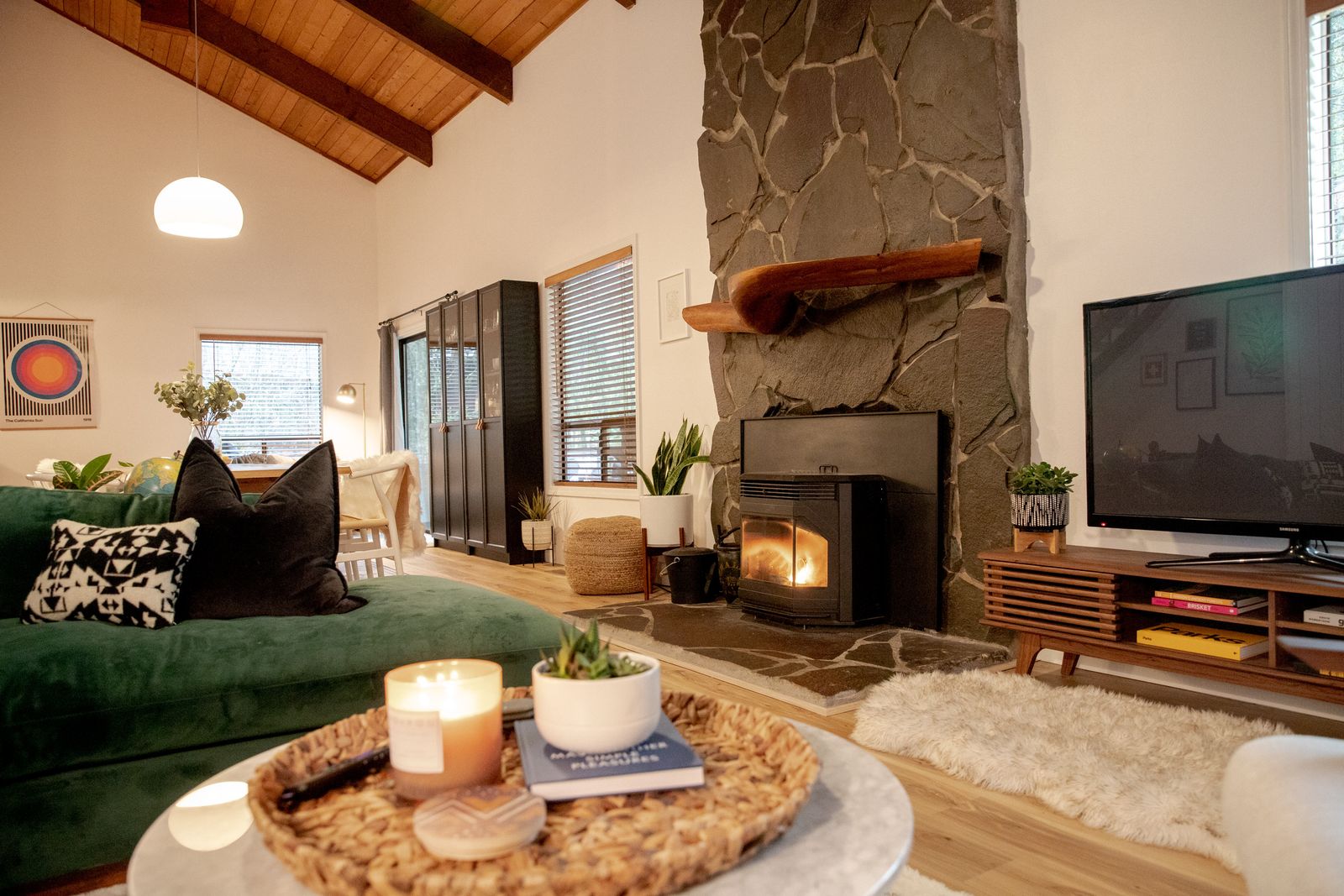 Living room with a green velvet sofa, stone pellet fireplace and vaulted wood ceiling